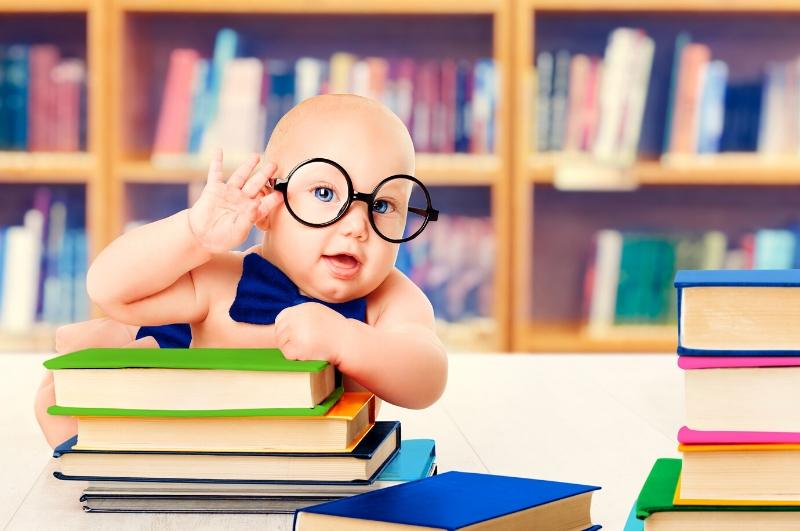 Baby with large glasses and a bow tie propped up over a stack of books