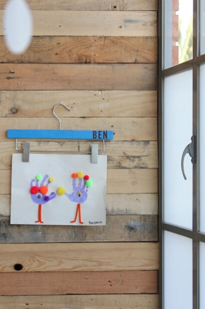 skirt hanger hanging on a wall holding a child's artwork
