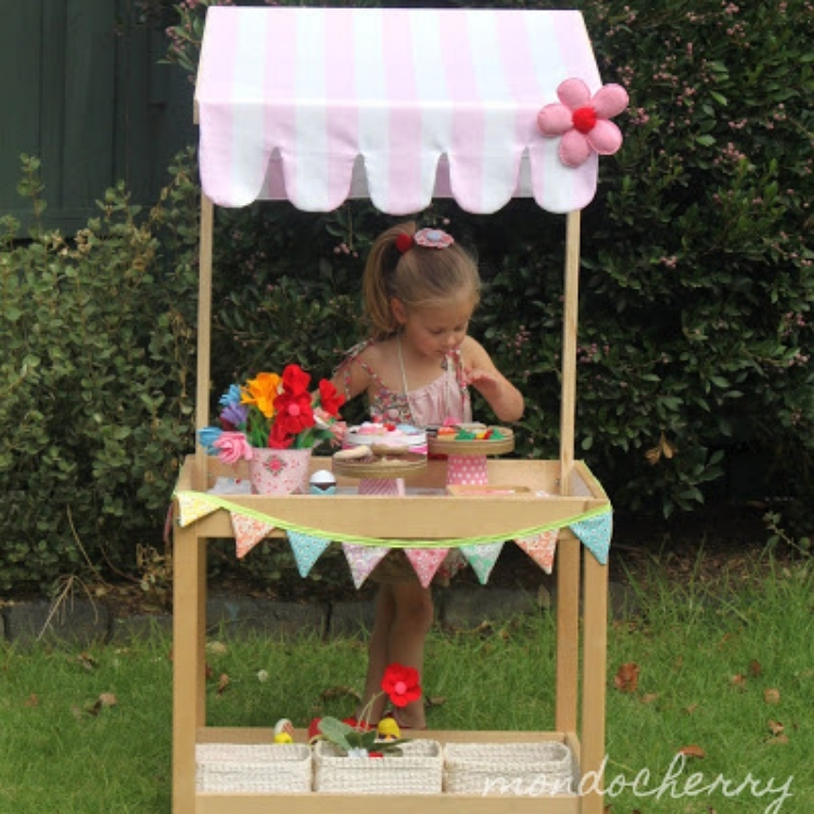 Little girl standing at repurposed changing tables transformed into outdoor play table with pink canopy