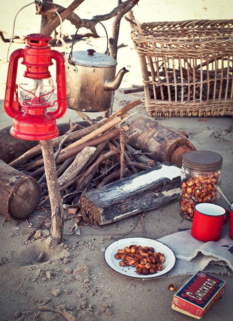 cold-weather-camping image of a campfire, lantern, a plate with food, a tin mug, and a jar of food on the sand