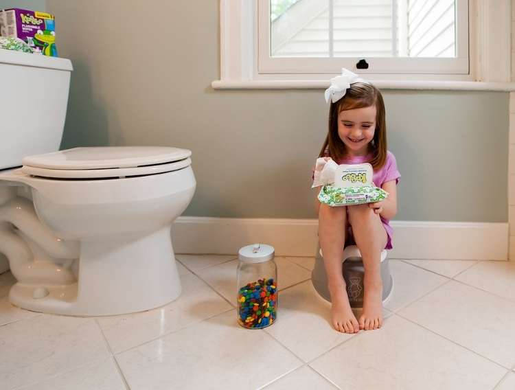 Little girl sitting in a bathroom next to a toilet, and a jar of candy