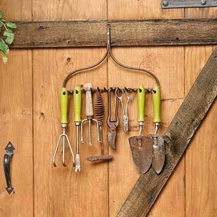 garden tools hanging from a repurposed old rake on the wall