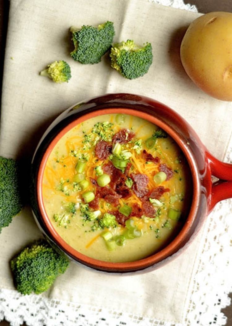 Instant Pot soup recipe for Cheddar Cheese Broccoli Potato Soup - with cheese, bacon, potatoes, and broccoli all served up in a creamy soup in a red ceramic bowl with handle.