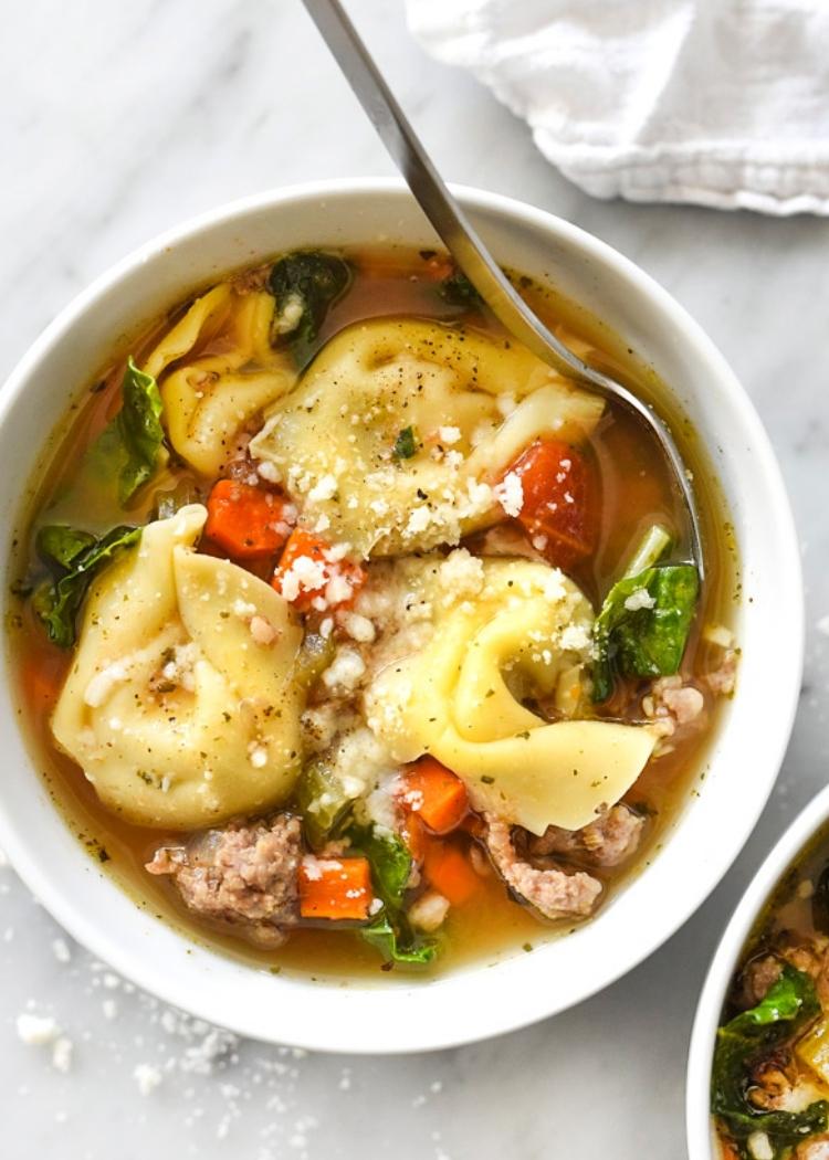 Slow Cooker Italian Tortellini Soup - flavoursome soup with large tortellini in a soup of sausage, onion, celery, and garlic - garnished with diced red peppers, green leaves and parmesan cheese on top. 