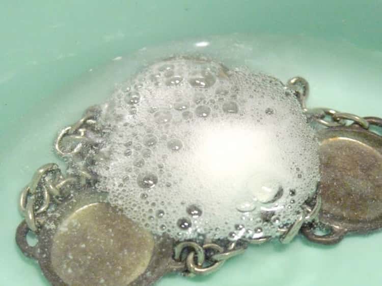 A photo of metal jewelry soaked in water and an alka-seltzer tablet dropped in it to remove tarnish