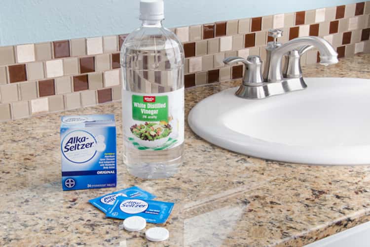 A photo of alka-seltzer tablets and a bottle of white vinegar beside a sink