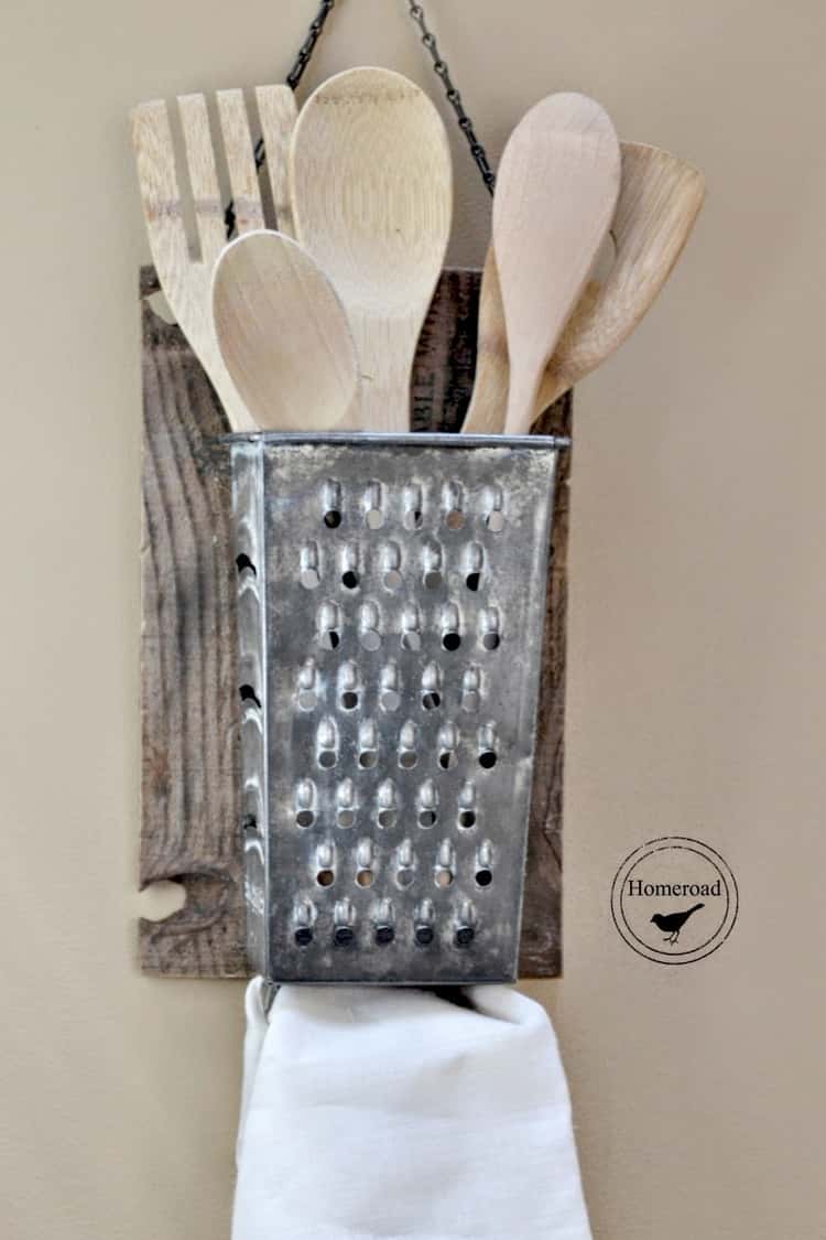 cheese grater turned into a utensil holder hanging on wall with kitchen spoons and forks inside