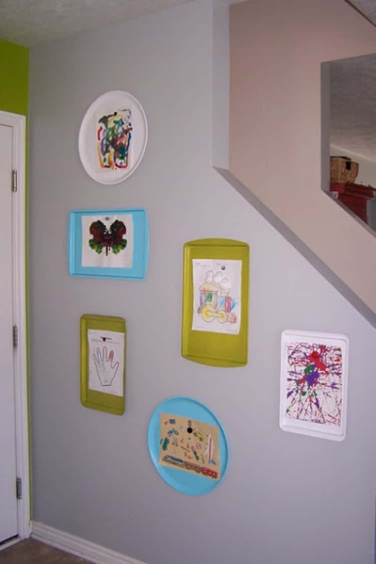 A colorful art wall for kids. The art pieces are hanging from cookie sheets of different shapes and colors 