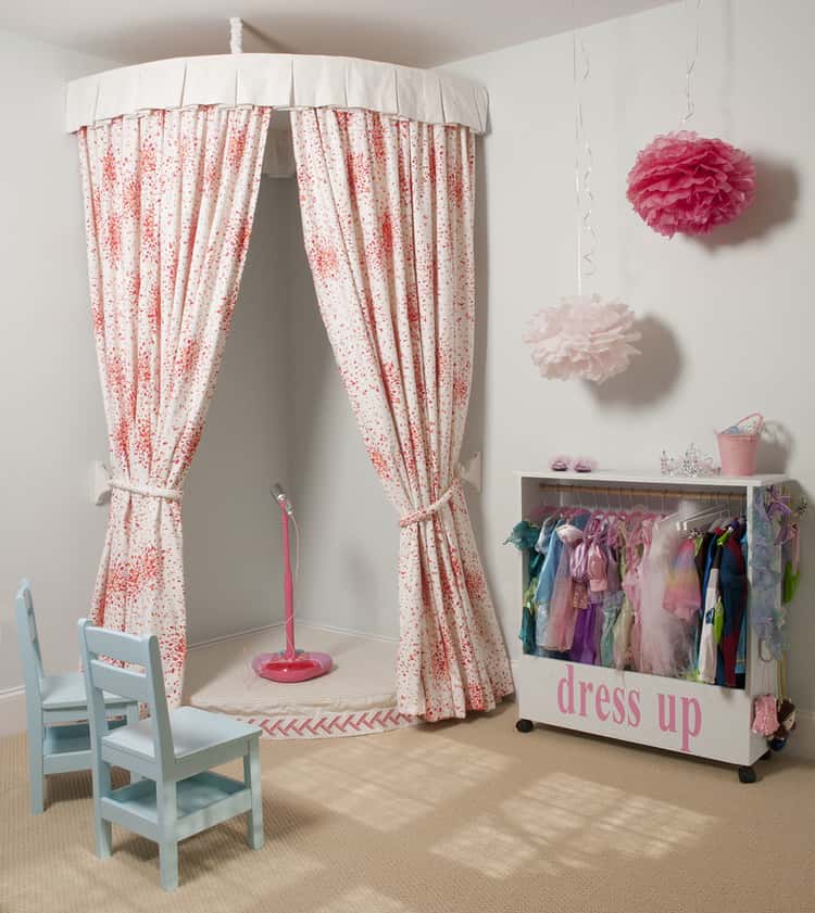 dress up corner with curtains hung from ceiling and a dress up box on the outside with little clothes in it. microphone in the middle too and small chairs.