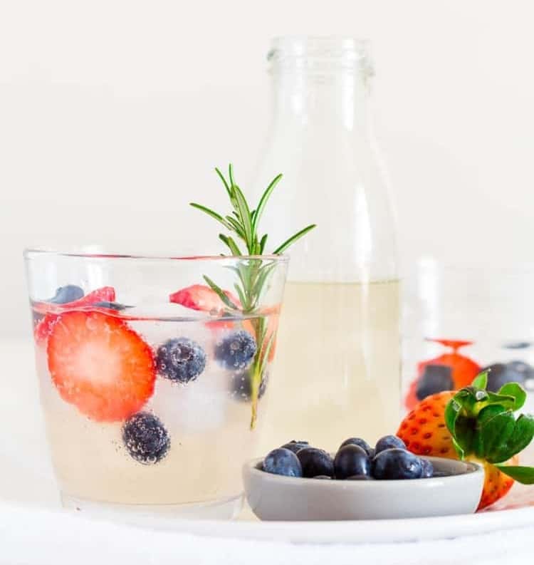 fruity lime and ginger beer mocktail garnished with rosemary sprig, strawberry slices, and some blackberries. 