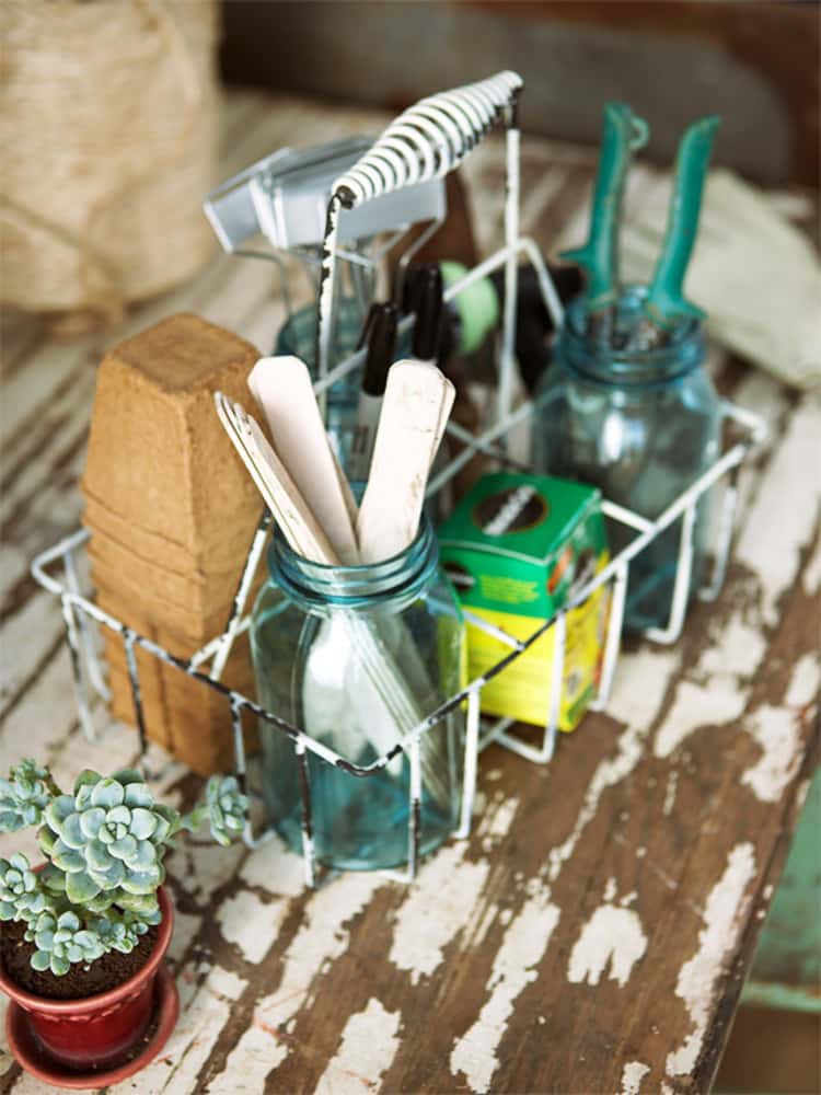 garden tools organized in a wire frame sitting on a wooden desk with a plant sitting next to it