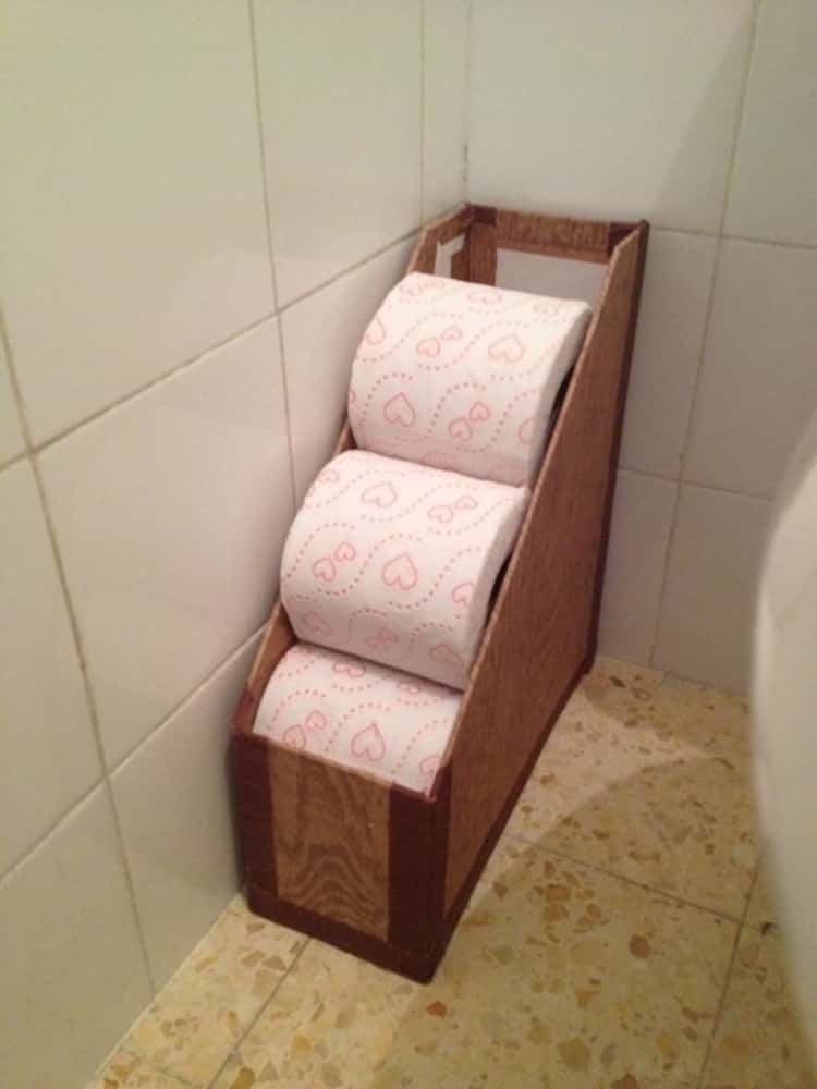 a magazine holder full of toilet rolls that's placed on the bathroom floor