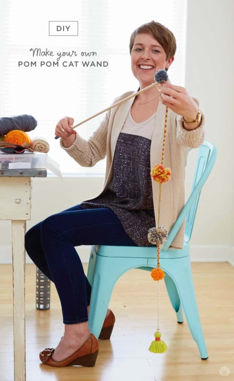 woman seated and holding a DIY pom-pom cat wand