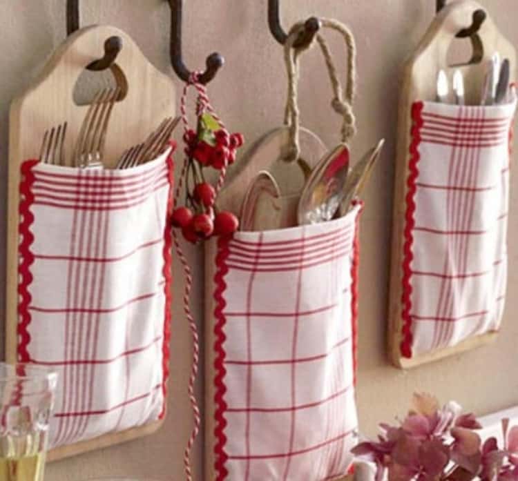 3 cutting boards with kitchen towels attached, hanging on the wall holding kitchen utensils