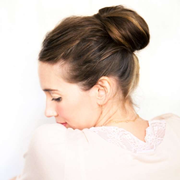  woman with brown hair looking over her shoulder, her hair is in a chestnut bun