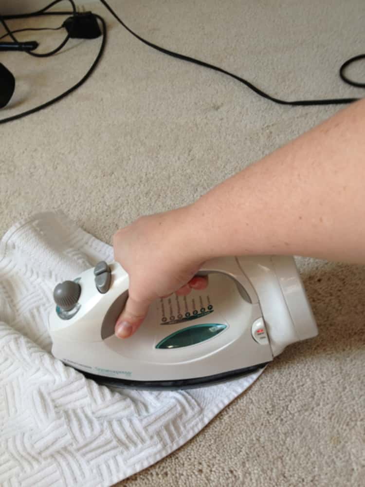 person ironing a towel on the carpet to clean a carpet stain 