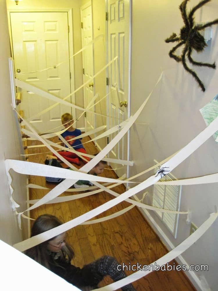 2 kids trying to make their way through a spider lair made from streamers and plastic spiders