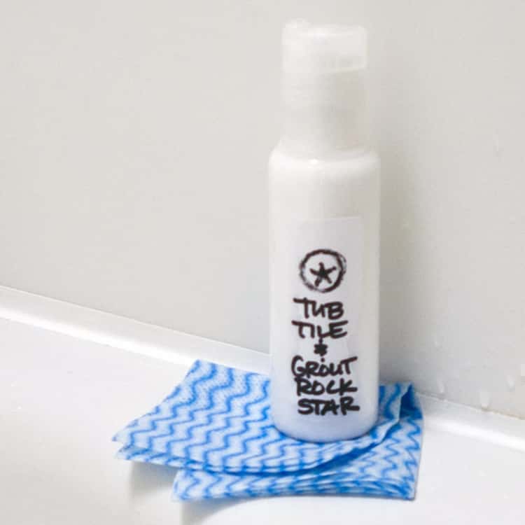 Bottle of homemade tub, tile and grout cleaner sitting on edge of tub with cleaning rag